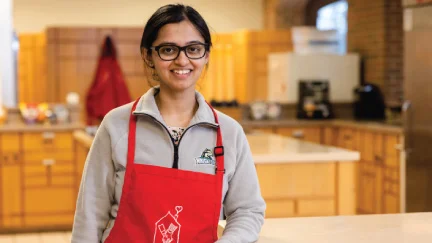 young adult female volunteer for RMHC Dayton smiling and wearing a red RMHC Dayton apron